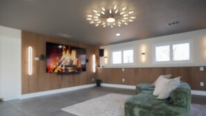 En moderne stue med en grøn sofa, et fladskærms-tv monteret på en trævæg og en loftlampe.