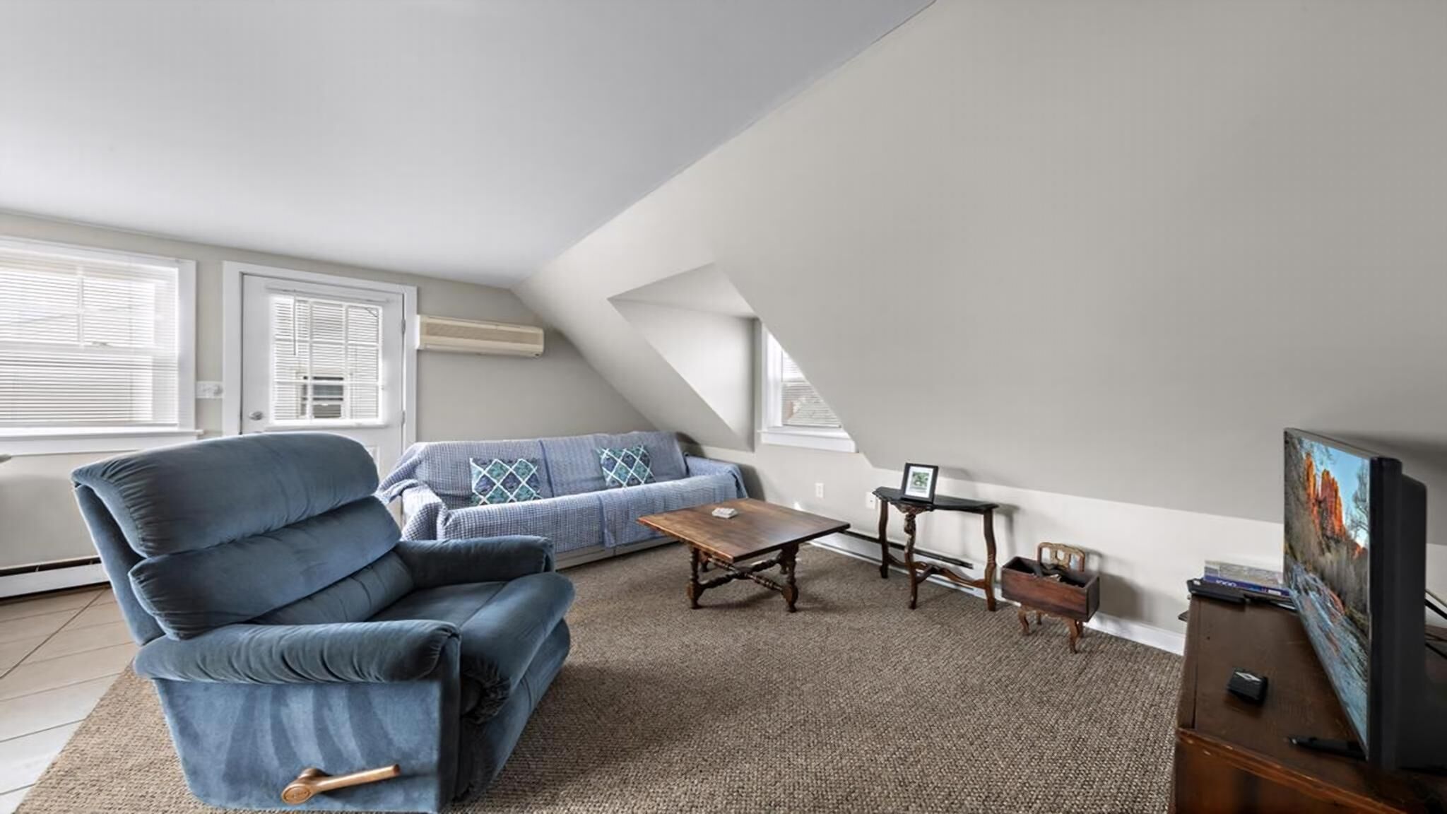 A loft-style living room with a blue sofa, a wooden coffee table, and a television on a wooden stand.