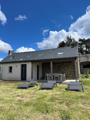 Une maison avec une façade en pierre, un toit plat et une terrasse amĂ©nagĂ©e avec du mobilier dâextĂ©rieur.