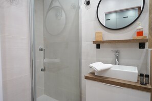 Ein modernes Badezimmer mit Duschkabine aus Glas, einem weißen Waschbecken und einem runden Spiegel.
