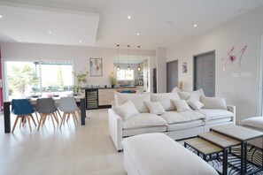 Una sala de estar moderna con un sofá blanco, un comedor con sillas, y una cocina al fondo.