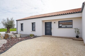 A modern house with a tiled roof, a gravel driveway, and a small garden with rocks and a tree. - Fauvette des sables - Jolie maison 3 chambres proche de la mer (Saint-Vincent-sur-Jard)