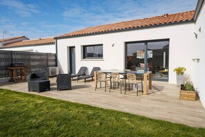 A modern patio with outdoor furniture, a barbecue, and a view of the house's interior through glass doors. - Fauvette des sables - Jolie maison 3 chambres proche de la mer (Saint-Vincent-sur-Jard)