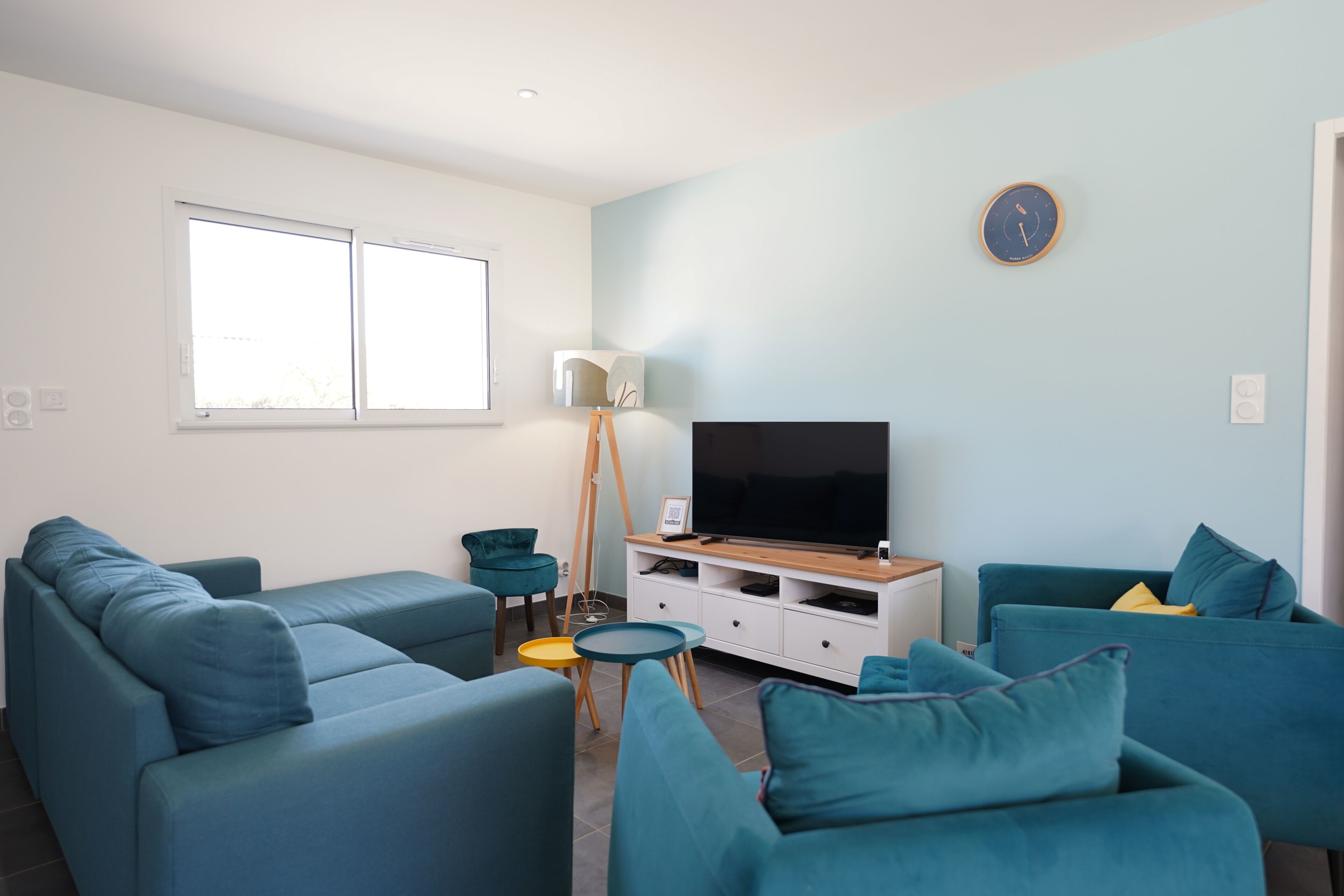 Ein modernes Wohnzimmer mit Flachbildfernseher, smaragdgrünen Sofas, einem kleinen runden Tisch und einer Stehlampe.