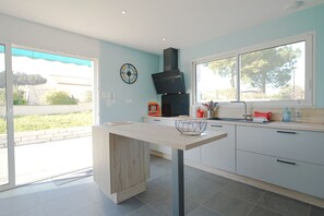 A modern kitchen with a wooden table, a black range hood, and a window with a view of greenery. - Longebeach - Three Bedroom House, Sleeps 6 (Longeville-sur-Mer)