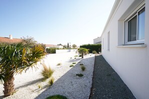 A residential area with a white building, a gravel pathway, and a palm tree. - Longebeach - Three Bedroom House, Sleeps 6 (Longeville-sur-Mer)