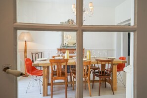 Un coin repas avec une table en bois dressée pour quatre personnes, entourée de chaises, et un lustre au-dessus.