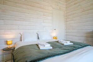 Ein Schlafzimmer mit Holzwandverkleidung, einem Bett mit weißer Bettwäsche, zwei Nachttischlampen und einer grünen Tagesdecke.
