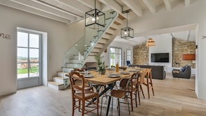 Un amplio salón con una mesa de comedor, sillas, una escalera y una pared de piedra.