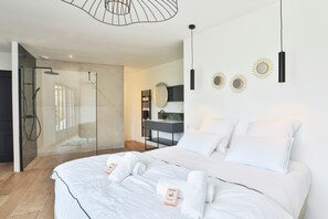 Ein modernes Schlafzimmer mit einem großen Bett, einer Duschkabine und einem Schminktisch mit Spiegel.