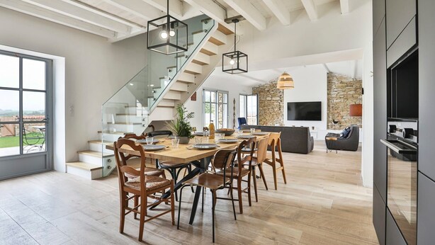 Amplia sala de estar con una mesa de comedor, sillas, una escalera y una pared de piedra.