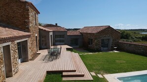 Una casa de piedra con terraza de madera, piscina y jardín con césped.