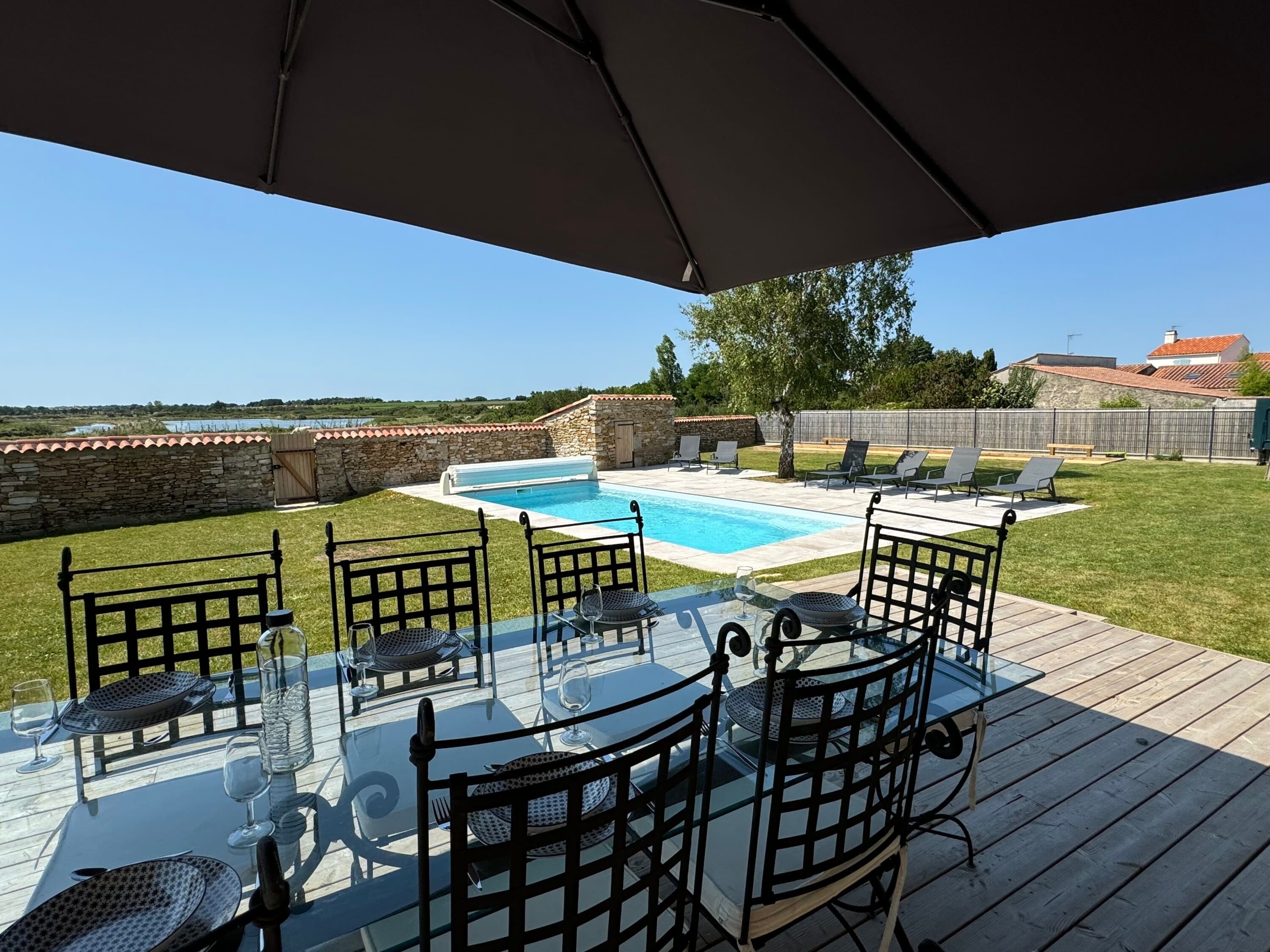 Una terraza con mesa y sillas de vidrio, una piscina y un muro de piedra.