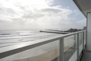 A balcony with a view of the beach and ocean, a pier, and buildings in the distance. - Aigue Marine - avec vue spectaculaire sur l'océan (Les Sables d'Olonne)