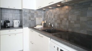 A modern kitchen with white cabinets, a black sink, and a tiled backsplash. - Aigue Marine - avec vue spectaculaire sur l'océan (Les Sables d'Olonne)