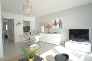 Ein modernes Wohnzimmer mit Essbereich, einem Fernseher und einer Küche im Hintergrund.