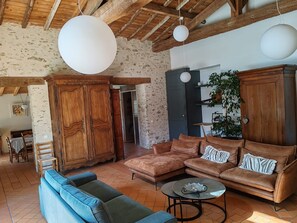 A rustic interior with exposed wooden beams, a stone wall, a brown leather sofa, a blue sofa, and a round coffee table. - Le Cottage du Fenestreau (Les Sables d'Olonne)