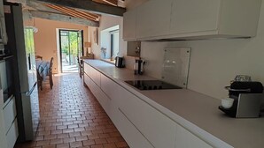 Ett kök med vita skåp, ett tegelgolv och utsikt över en matplats utomhus.