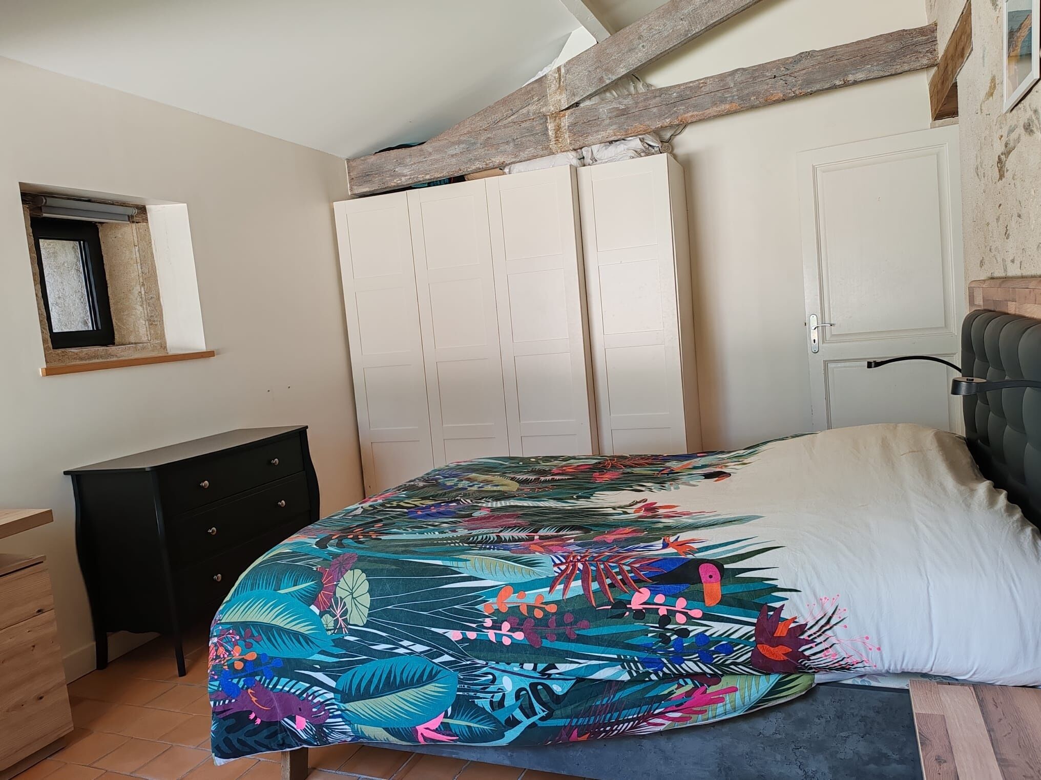 A bedroom with a bed, a dresser, a wardrobe, and a window.