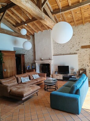 A rustic living room with exposed wooden beams, a fireplace, a television, and a large hanging light fixture. - Le Cottage du Fenestreau (Les Sables d'Olonne)