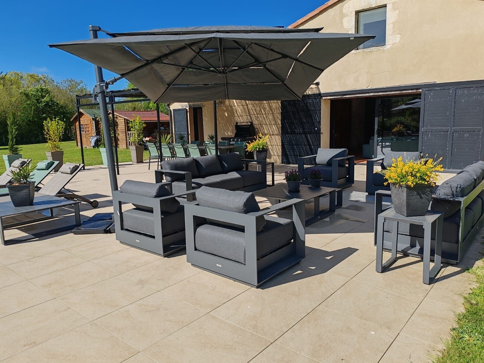An outdoor patio with modern furniture, a large umbrella, and a view of a house in the background.