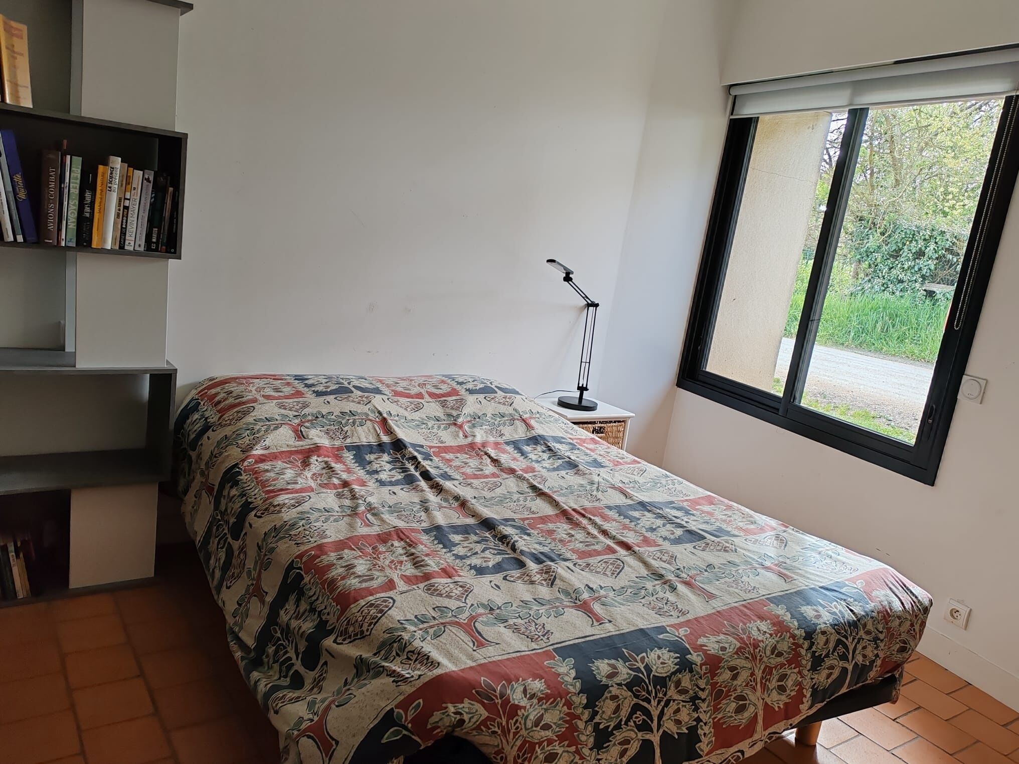 A bedroom with a bed, a bookshelf, a desk, and a window.