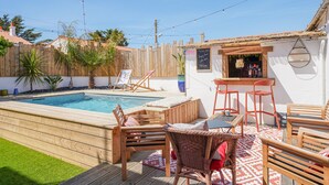 Ein Garten mit Schwimmbecken, Holzterrasse, Sitzgelegenheiten im Freien und einer Bar.