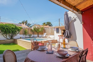 A patio with a table set for dining, a pool, and a red wall. - Villa Parisse - Five Bedroom House, Sleeps 9 (Les Sables d'Olonne)