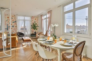 A dining area with a round table, chairs, and a view through large windows. - Villa Parisse - Five Bedroom House, Sleeps 9 (Les Sables d'Olonne)