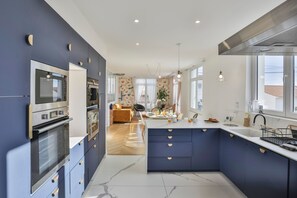 A modern kitchen with built-in ovens, a central island, and a dining area with a sofa. - Villa Parisse - Five Bedroom House, Sleeps 9 (Les Sables d'Olonne)
