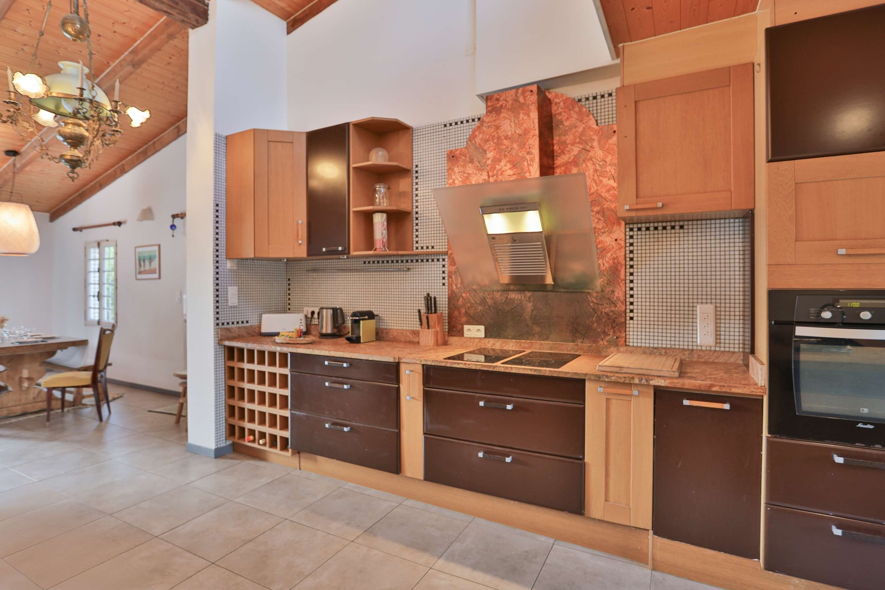 A modern kitchen with wooden cabinets, a built-in oven, and a large island with a sink.