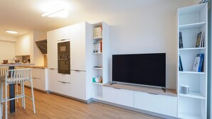 A modern kitchen with built-in appliances, a flat-screen TV, and a dining area with bar stools. - Beluga - pied-à-terre idéal sur la côte vendéenne (Les Sables d'Olonne)
