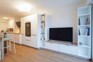A modern kitchen with built-in appliances, a flat-screen TV, and a dining area with bar stools. - Beluga - One Bedroom Apartment, Sleeps 4 (Les Sables d'Olonne)