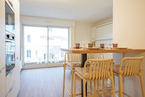 A modern kitchen with a dining table and chairs, a large window, and a view of buildings outside. - Beluga - One Bedroom Apartment, Sleeps 4 (Les Sables d'Olonne)