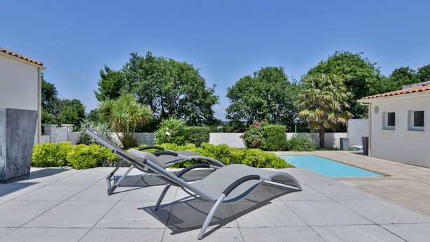 Un espace aménagé au bord de la piscine, avec des chaises longues, une piscine et une végétation luxuriante tout autour.