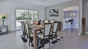 Un coin repas avec une table dressée pour quatre personnes, des chaises, un vase rempli de fleurs et une vue à travers la porte vitrée.