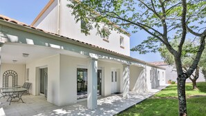 Un bâtiment blanc doté d’un patio couvert, d’une entrée avec une porte vitrée et d’un arbre au premier plan.