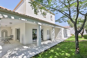 A white building with a covered patio, a glass door entrance, and a tree in the foreground. - L'Orangerie des Sables (Les Sables d'Olonne)