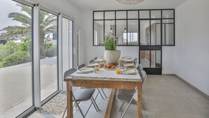A dining area with a large table set for six, a potted plant, and a view through glass doors. - Villa Mediterranée - Three Bedroom House, Sleeps 8 (Les Sables d'Olonne)