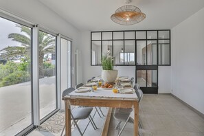 A dining area with a large table set for six, a potted plant, and a view through glass doors. - Villa Mediterranée - Three Bedroom House, Sleeps 8 (Les Sables d'Olonne)