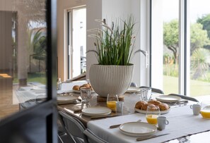 A dining table set with plates, glasses, and croissants, with a large white bowl of green plants in the center. - Villa Mediterranée - Three Bedroom House, Sleeps 8 (Les Sables d'Olonne)