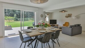 Un espace de restauration moderne, doté d’une grande table, de chaises et offrant une vue sur le jardin grâce à de grandes portes vitrées.