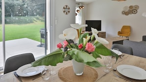 Un coin repas avec une table dressée pour deux personnes, une plante en pot et une vue sur l’extérieur.