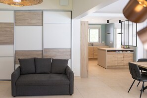 Ein modernes Wohnzimmer mit einer Couch, einem Esstisch mit Stühlen und einer Küchenzeile im Hintergrund.