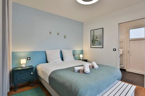 A neatly made bed with a blue headboard, a bedside table with a lamp, and a framed picture on the wall. - Quai Ouest - élégante maison avec piscine (Saint-Vincent-sur-Jard)