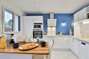 A modern kitchen with white cabinets, a wooden countertop, a built-in oven, a microwave, and a sink with a gold faucet. - Quai Ouest - élégante maison avec piscine (Saint-Vincent-sur-Jard)