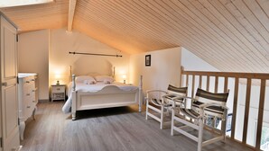 Una camera da letto con soffitto in legno, un letto, un comodino, una cassettiera e due sedie.