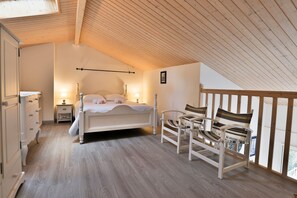 Ein Schlafzimmer mit Holzboden, einem Bett, einem Nachttisch, einer Kommode und zwei Stühlen.