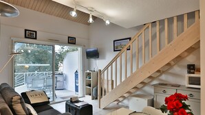 Una moderna camera d'albergo con una scala in legno, un divano, un tavolo da pranzo apparecchiato con bicchieri e una televisione.