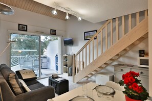Ein modernes Hotelzimmer mit einer Holztreppe, einem Sofa, einem Esstisch mit Gläsern und einem Fernseher.